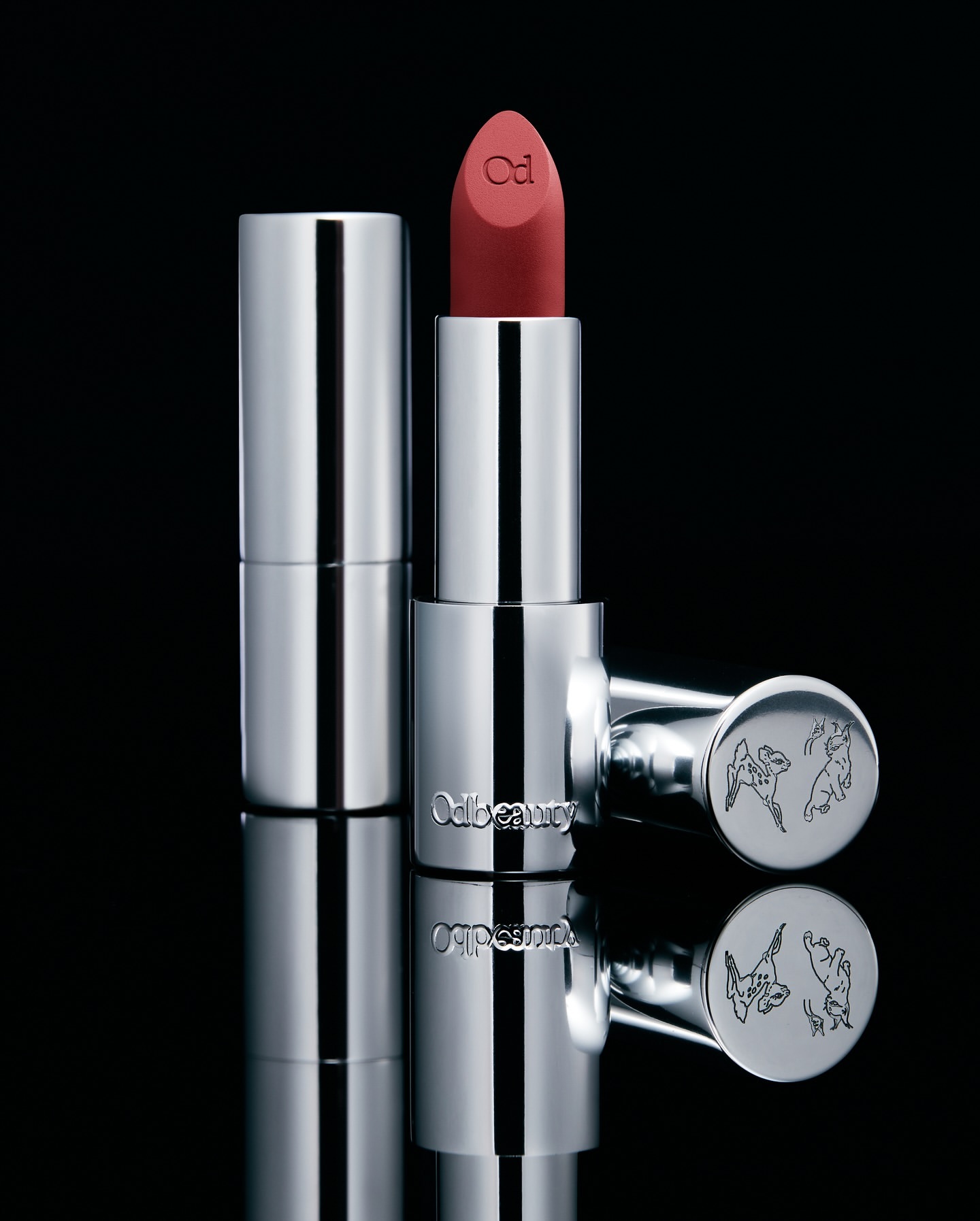 Studio shot of Odile Monod Beauty silver lipstick tube, showcasing the product's design and color against a dark reflective background.