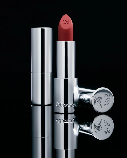 Studio shot of Odile Monod Beauty silver lipstick tube, showcasing the product's design and color against a dark reflective background.