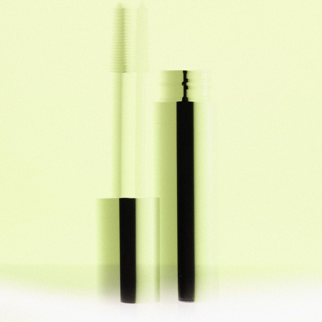 Beauty shot of mascara and wand applicator with reflective silver accents on a light yellow background, clean and minimalist.