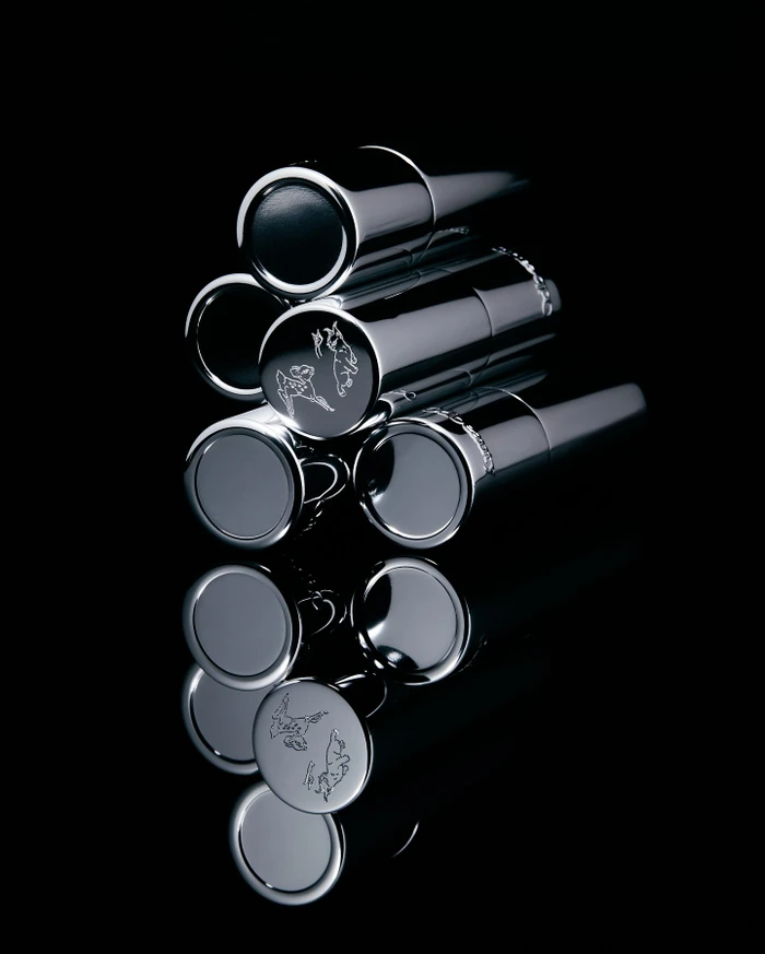 Close-up of polished silver lipstick tubes stacked neatly against a deep black background with a clean glossy reflection below.