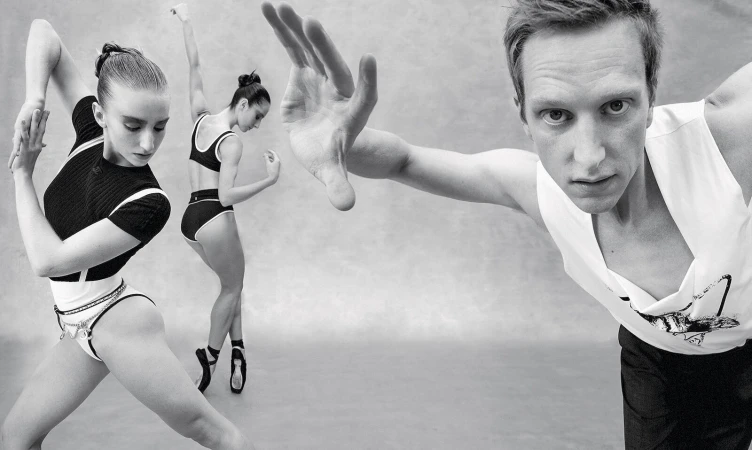 Monochrome image of a male dancer in the foreground with outstretched hand and two female dancers posing in the background.