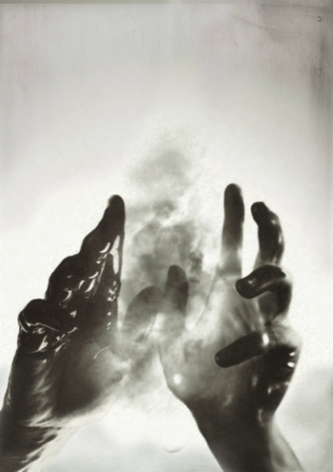 Monochrome photograph featuring two hands reaching up against a bright background, creating a high-contrast, abstract and surreal effect.