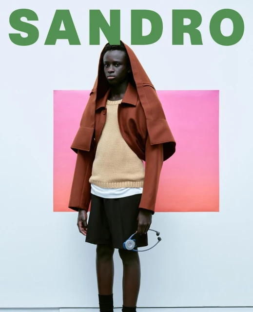 Fashionable adult male model showcases Sandro apparel in a studio shot, posing with a stethoscope, set against a gradient backdrop.