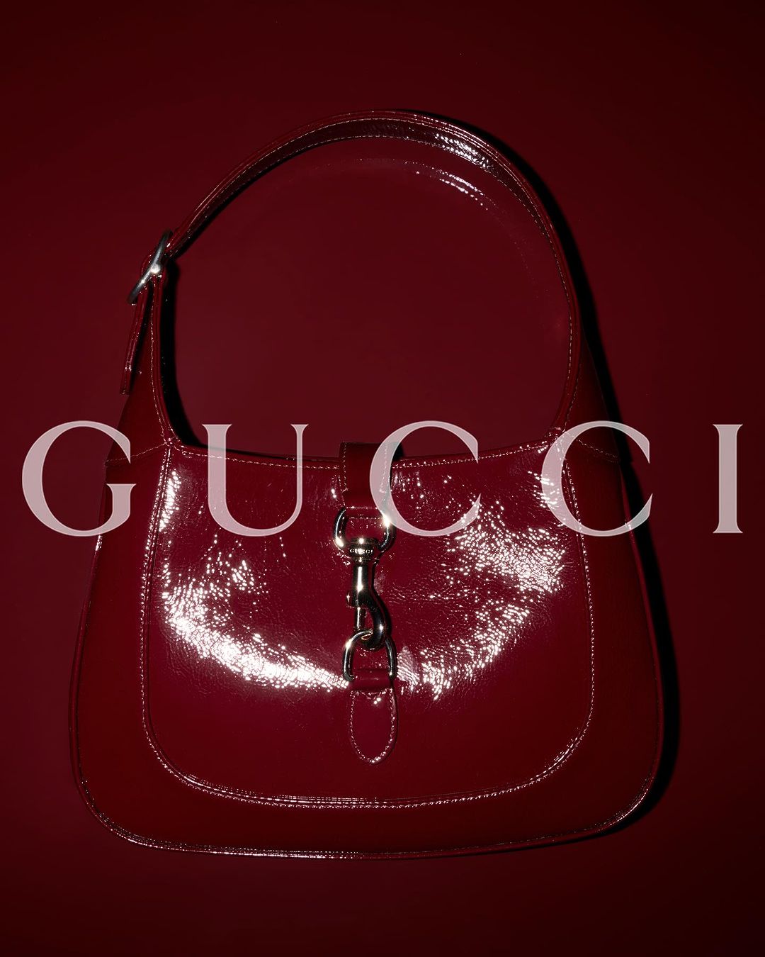 Burgundy Gucci Jackie bag on a matching background with a reflective, glossy surface and silver hardware.