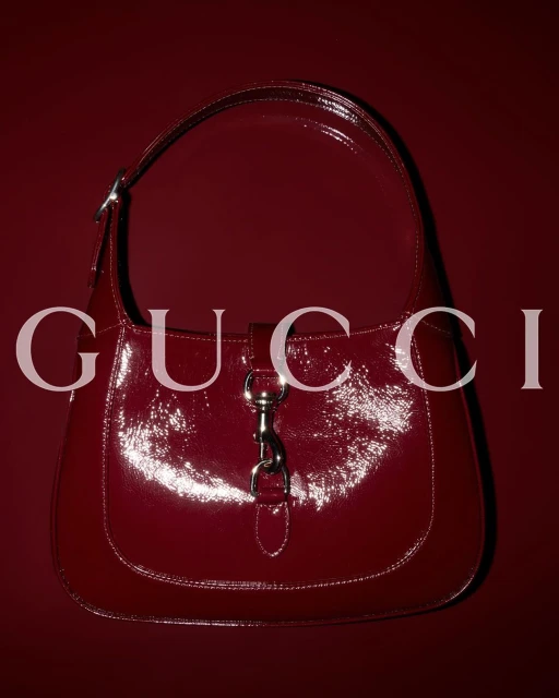 Burgundy Gucci Jackie bag on a matching background with a reflective, glossy surface and silver hardware.