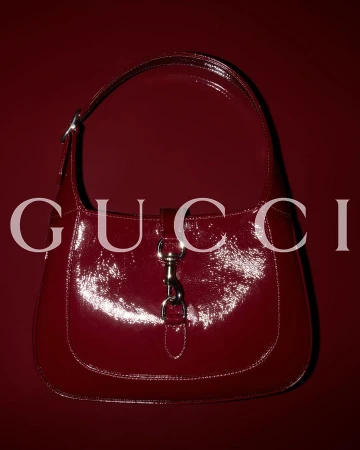 Burgundy Gucci Jackie bag on a matching background with a reflective, glossy surface and silver hardware.
