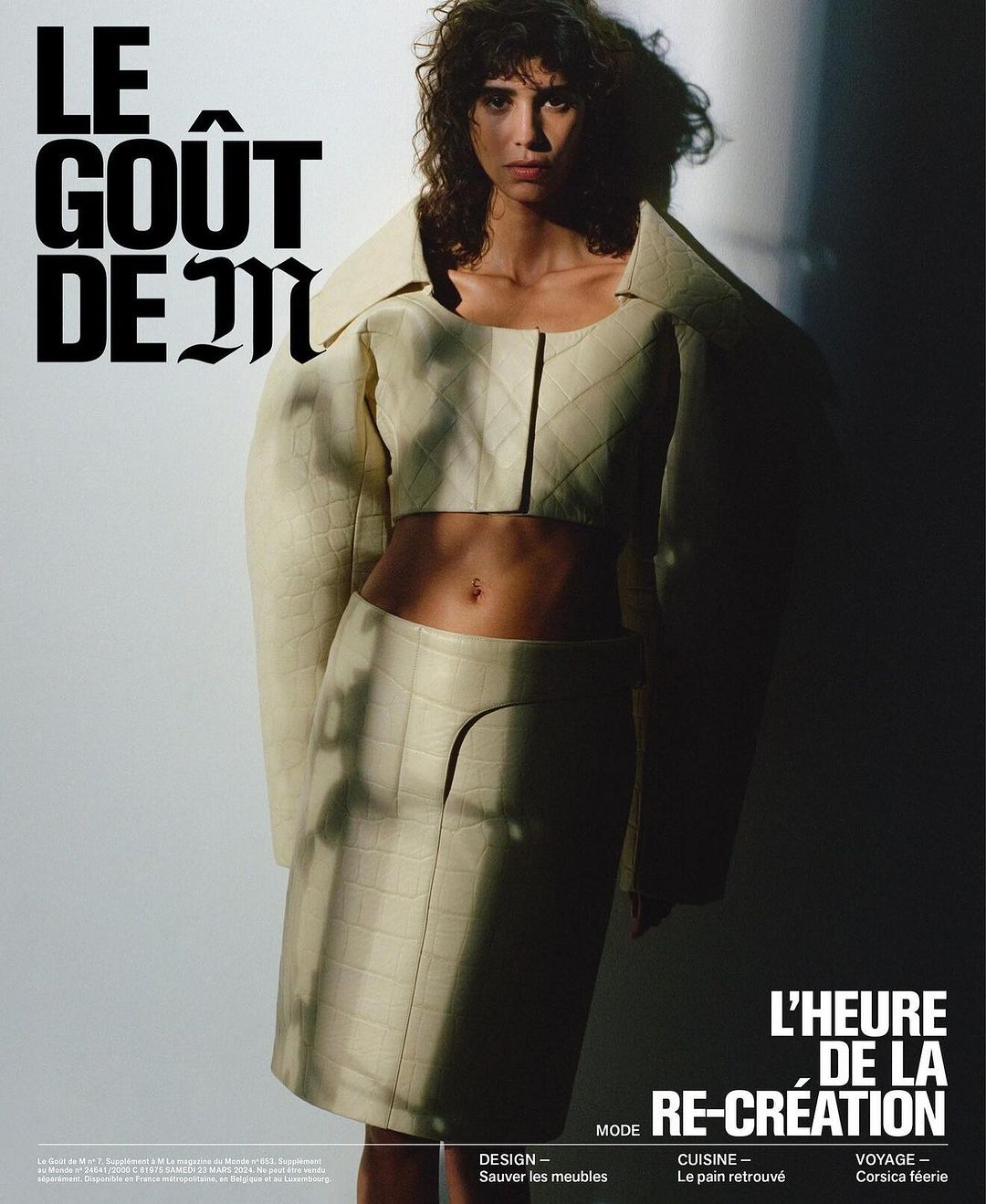 Fashion editorial image of a woman in a cream quilted jacket and skirt, posing in a studio with dramatic lighting and bold typography.
