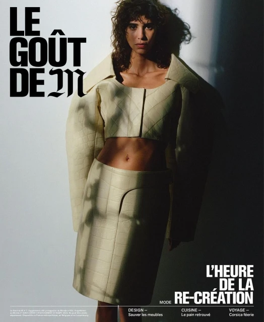 Fashion editorial image of a woman in a cream quilted jacket and skirt, posing in a studio with dramatic lighting and bold typography.