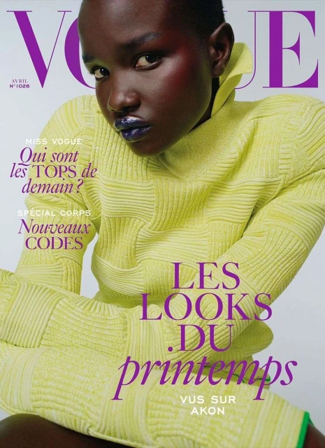 Vogue cover featuring a black model in a bright yellow outfit. The model has dark skin and purple lipstick, and the cover has purple Vogue text.