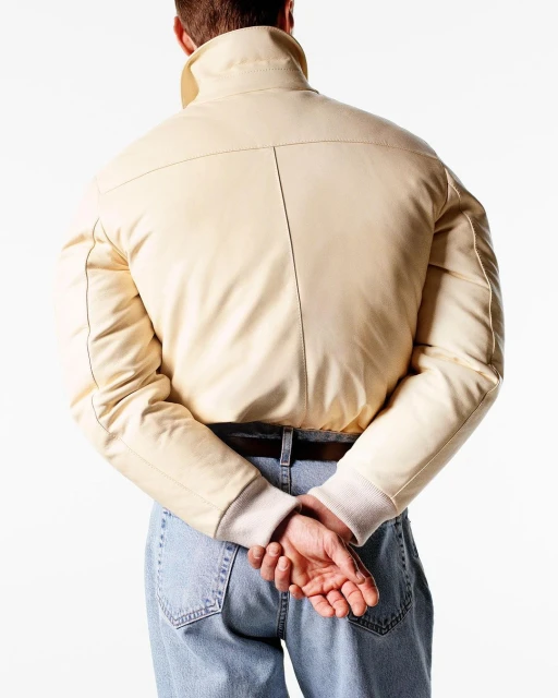 Back view of a person wearing a cream-colored jacket and blue jeans against a white background, showcasing fashion apparel.