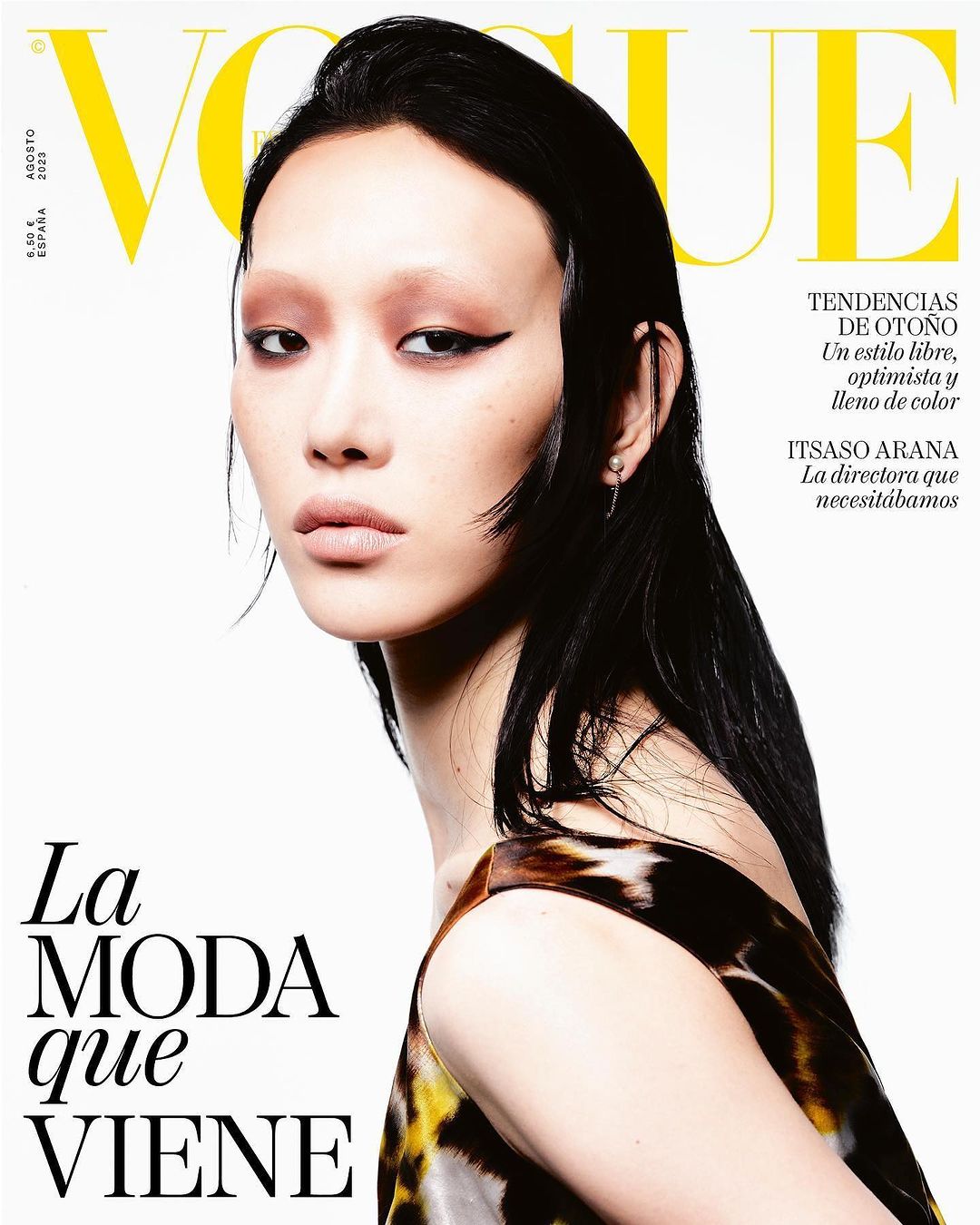 Close-up portrait of a model with dark wet-look hair and graphic eyeliner against a white background for a magazine cover.