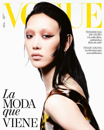 Close-up portrait of a model with dark wet-look hair and graphic eyeliner against a white background for a magazine cover.