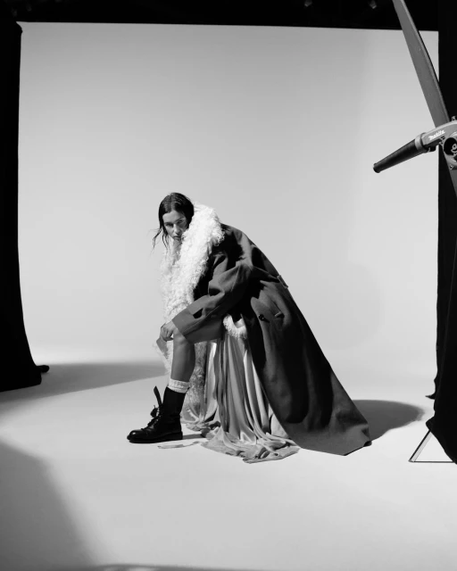 Monochrome fashion portrait of a woman in a coat with fur trim, posing in a photo studio with vintage film lighting equipment.