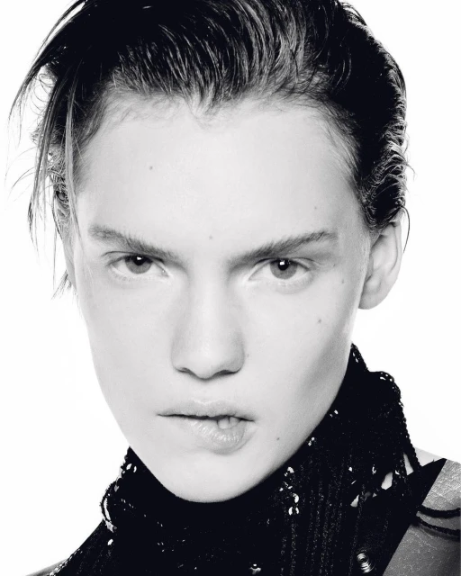 Close-up black and white portrait of a young adult woman with short dark hair, wearing a dark, sequined top against a white background.