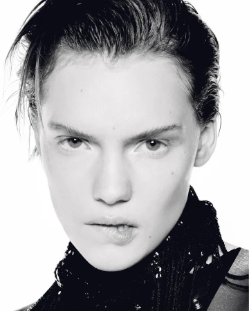 Close-up black and white portrait of a young adult woman with short dark hair, wearing a dark, sequined top against a white background.