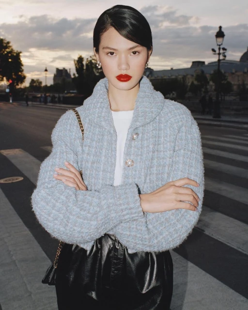 Woman posing outdoors in a blue jacket and black skirt, city street with building and street lights in the background at dusk.