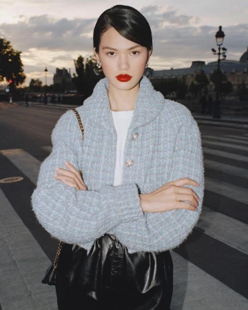 Woman posing outdoors in a blue jacket and black skirt, city street with building and street lights in the background at dusk.