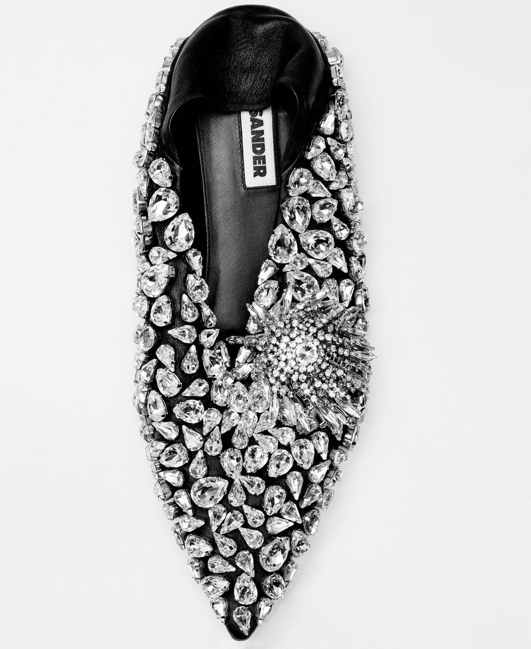 Black leather slipper with decorative crystal embellishments and a pointed toe, set against a plain white backdrop.