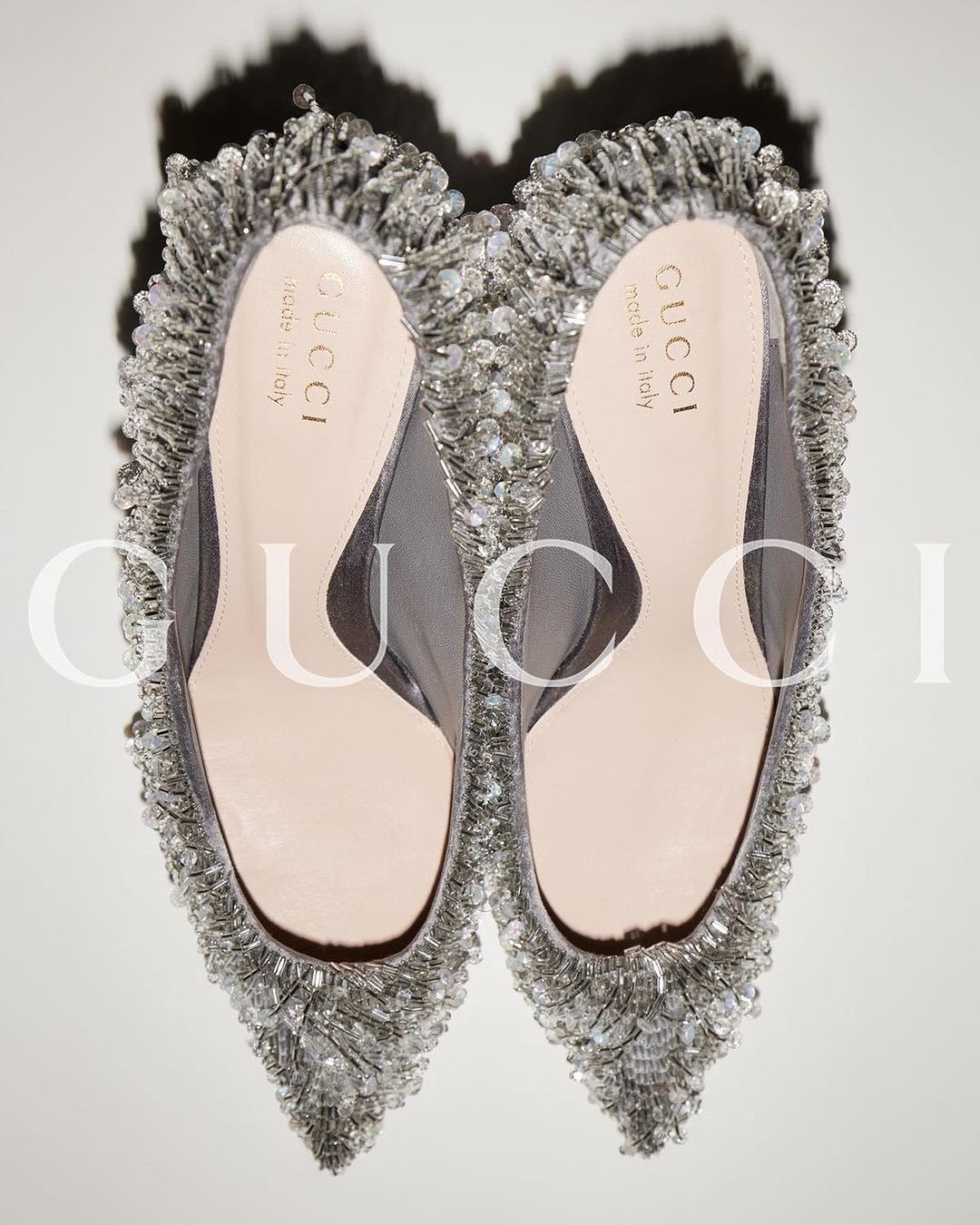 Close-up studio shot of a pair of silver-beaded Gucci heels with mesh and pale pink leather. Elegant designer fashion footwear.