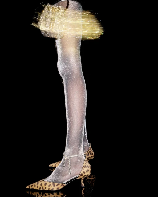 Legs wearing sparkling sheer tights and leopard print kitten heels, holding a glowing purse, on a black background.