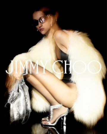 Crouching woman in sunglasses wearing a cream fur coat and silver sandals, holding a silver bag, photographed by Anthony Seklaoui.
