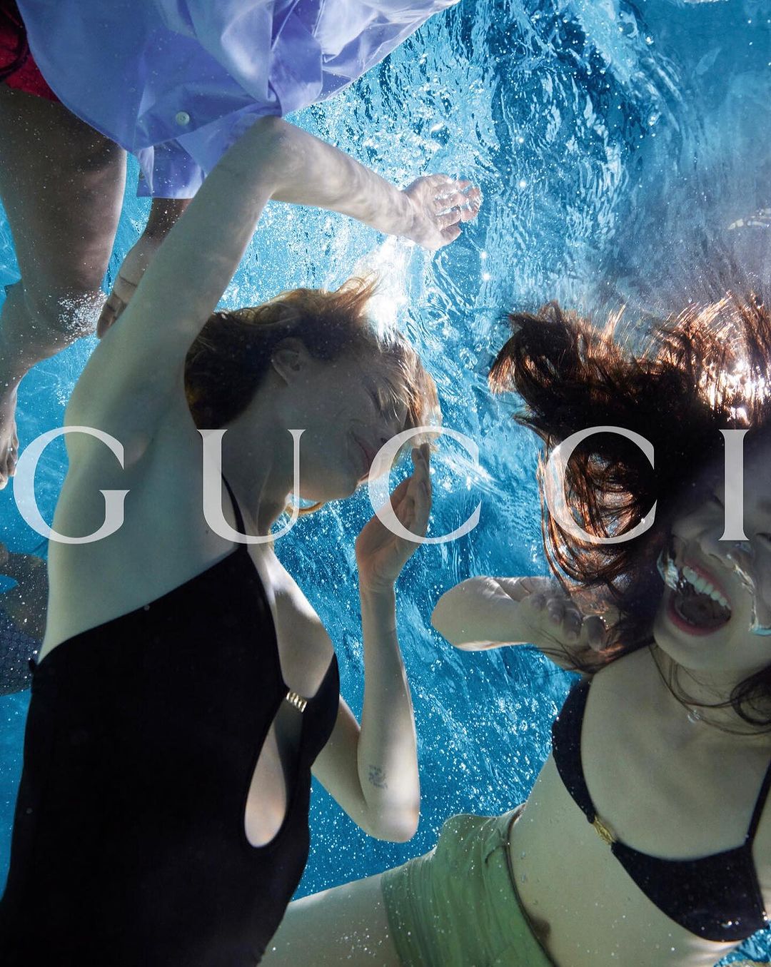 Three people in a pool wearing swimwear, with GUCCI logo in the foreground, creating a dynamic and fashionable underwater scene.