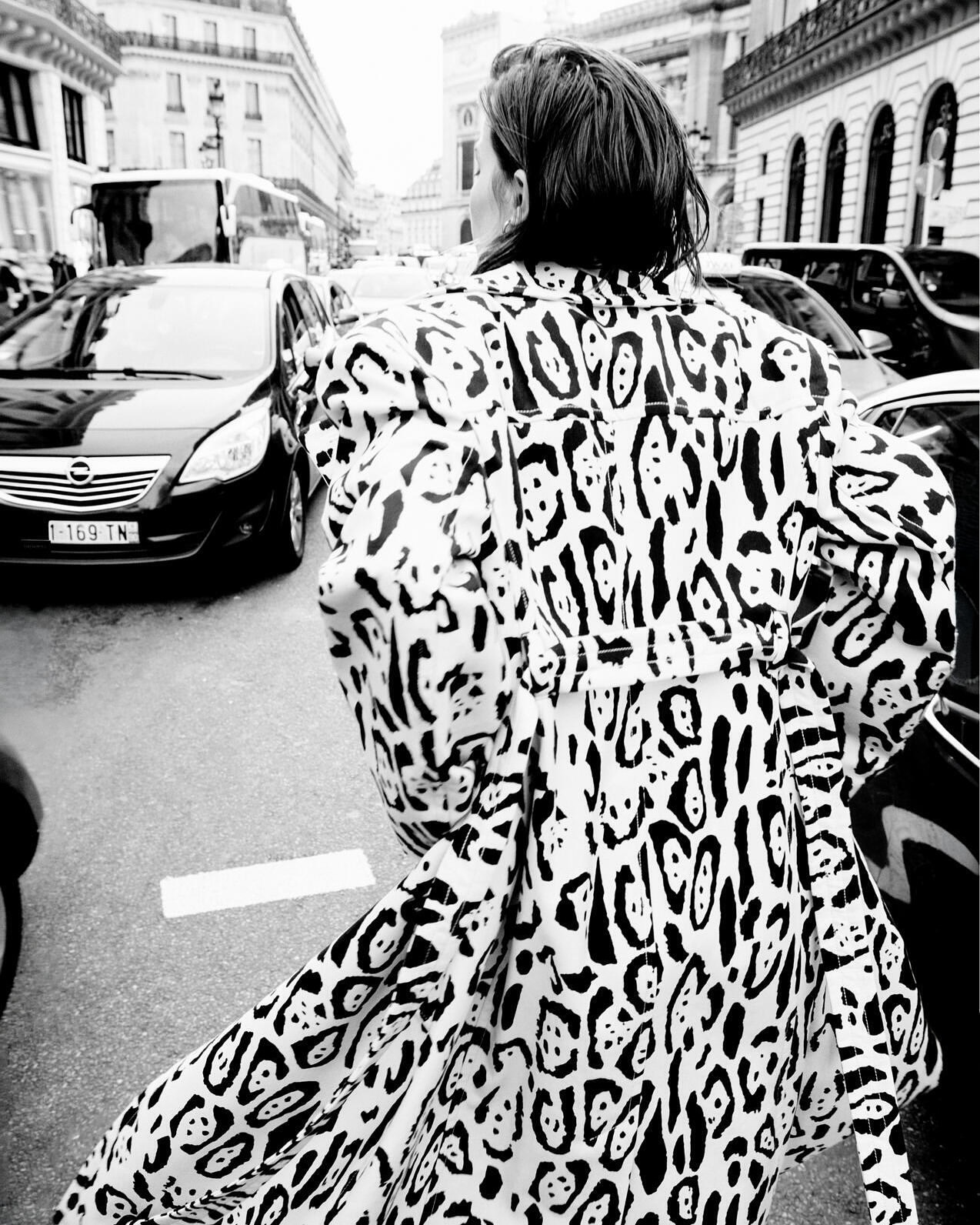 Model seen from behind walking down a busy city street wearing a bold black and white patterned trench coat.