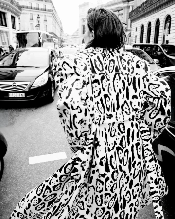 Model seen from behind walking down a busy city street wearing a bold black and white patterned trench coat.