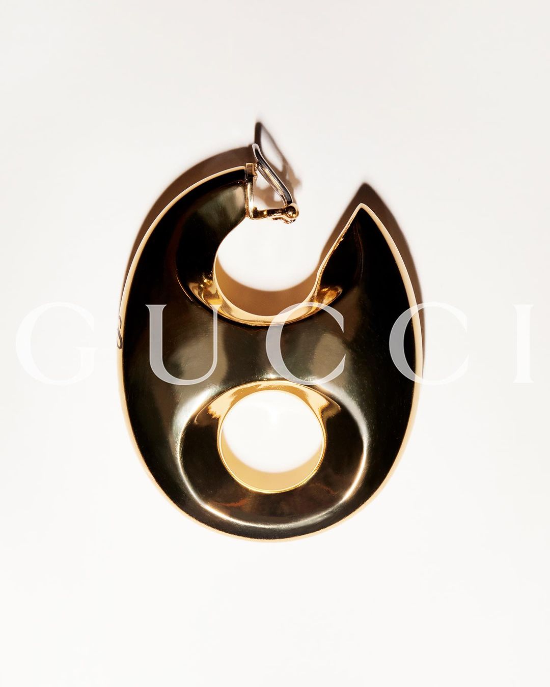 Single, bold gold earring on a white background, featuring a stylized, geometric design with a distinct circular cutout.