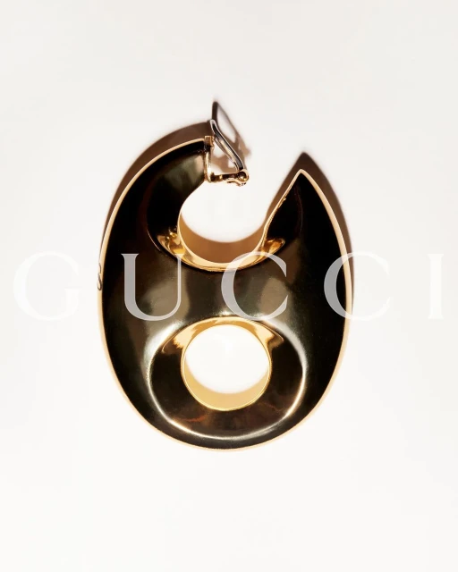 Single, bold gold earring on a white background, featuring a stylized, geometric design with a distinct circular cutout.
