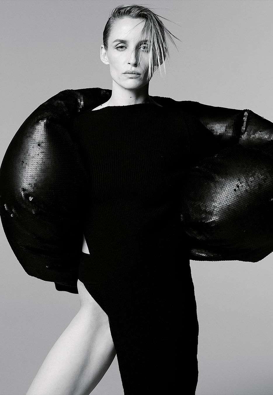 Woman with slicked hair wearing a black sculptural top against a plain grey background