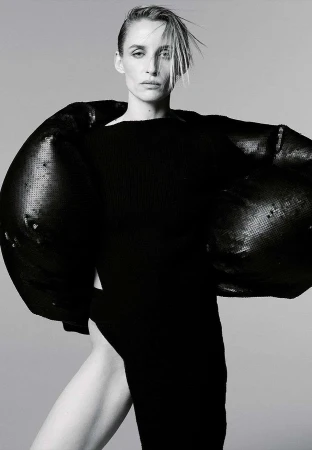 Woman with slicked hair wearing a black sculptural top against a plain grey background