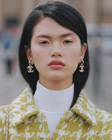 Close-up portrait of an East Asian woman wearing a tweed jacket, white turtleneck, and designer earrings photographed by Anthony Seklaoui.