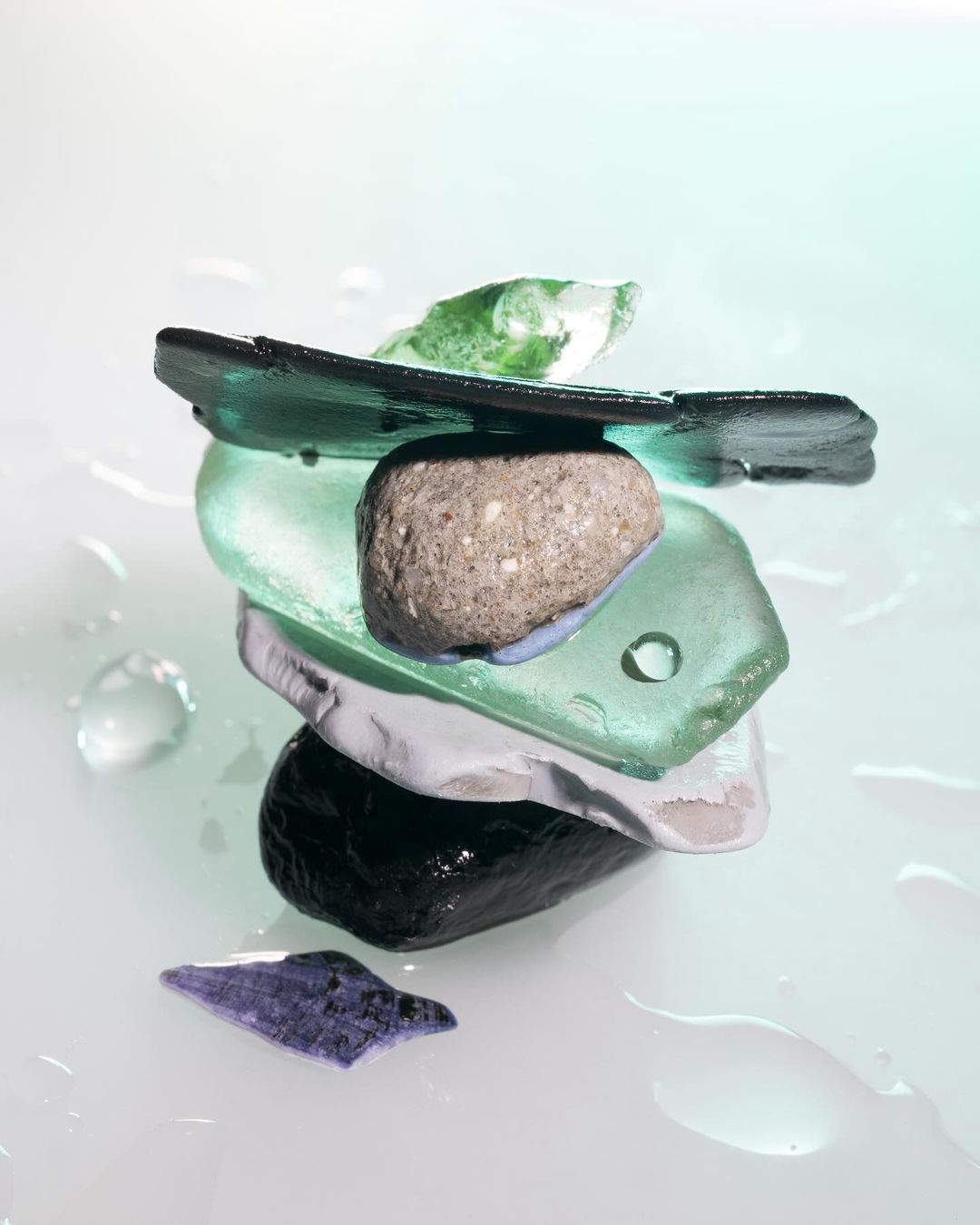 Stacked sea glass and stone tower formation on a white surface with water droplets. Close-up studio shot. 