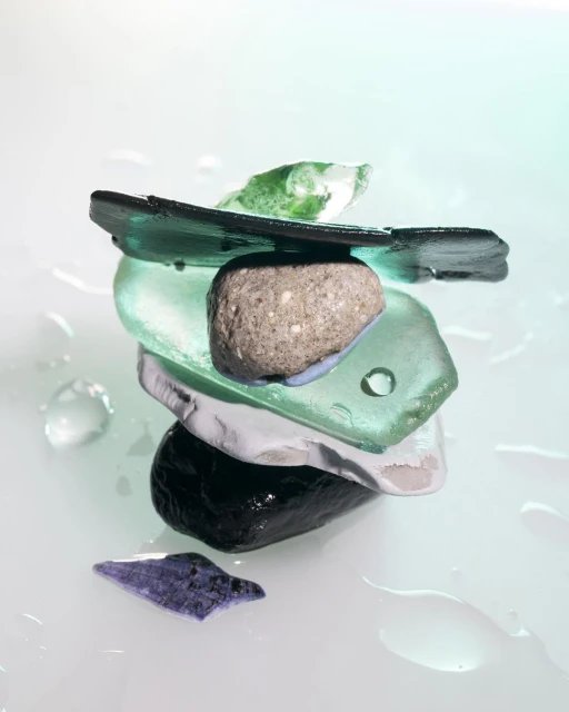 Stacked sea glass and stone tower formation on a white surface with water droplets. Close-up studio shot. 