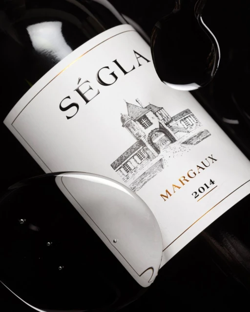 Close-up of a bottle of Séglà Margaux 2014 wine with water droplets against a black background, showcasing its label details and elegance.