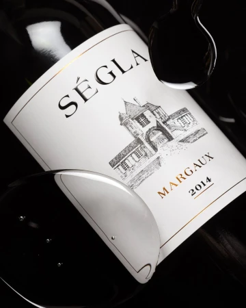 Close-up of a bottle of Séglà Margaux 2014 wine with water droplets against a black background, showcasing its label details and elegance.
