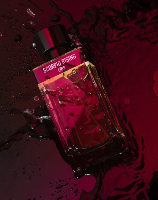Eris Scorpio Rising perfume bottle on a reflective dark surface with water droplets, product shot, beauty industry advertising.