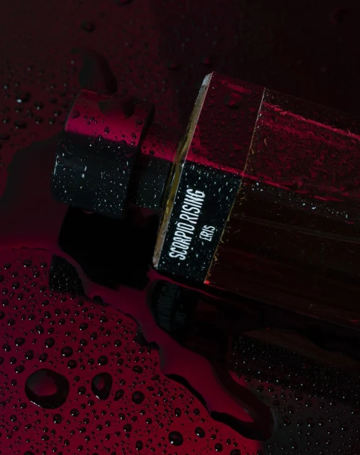 Product shot of Scorpio Rising Eris fragrance in a dark, moody setting with water droplets for a sensual, high-end product image.