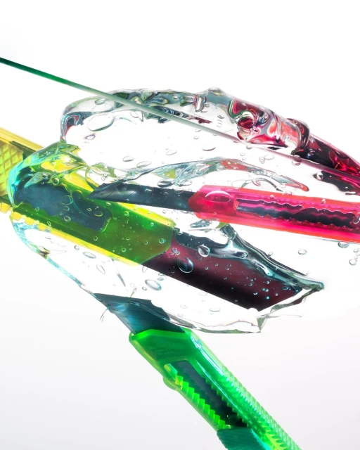 Colorful box cutter tools submerged in clear water under bright lighting, creating a visually striking and abstract composition.