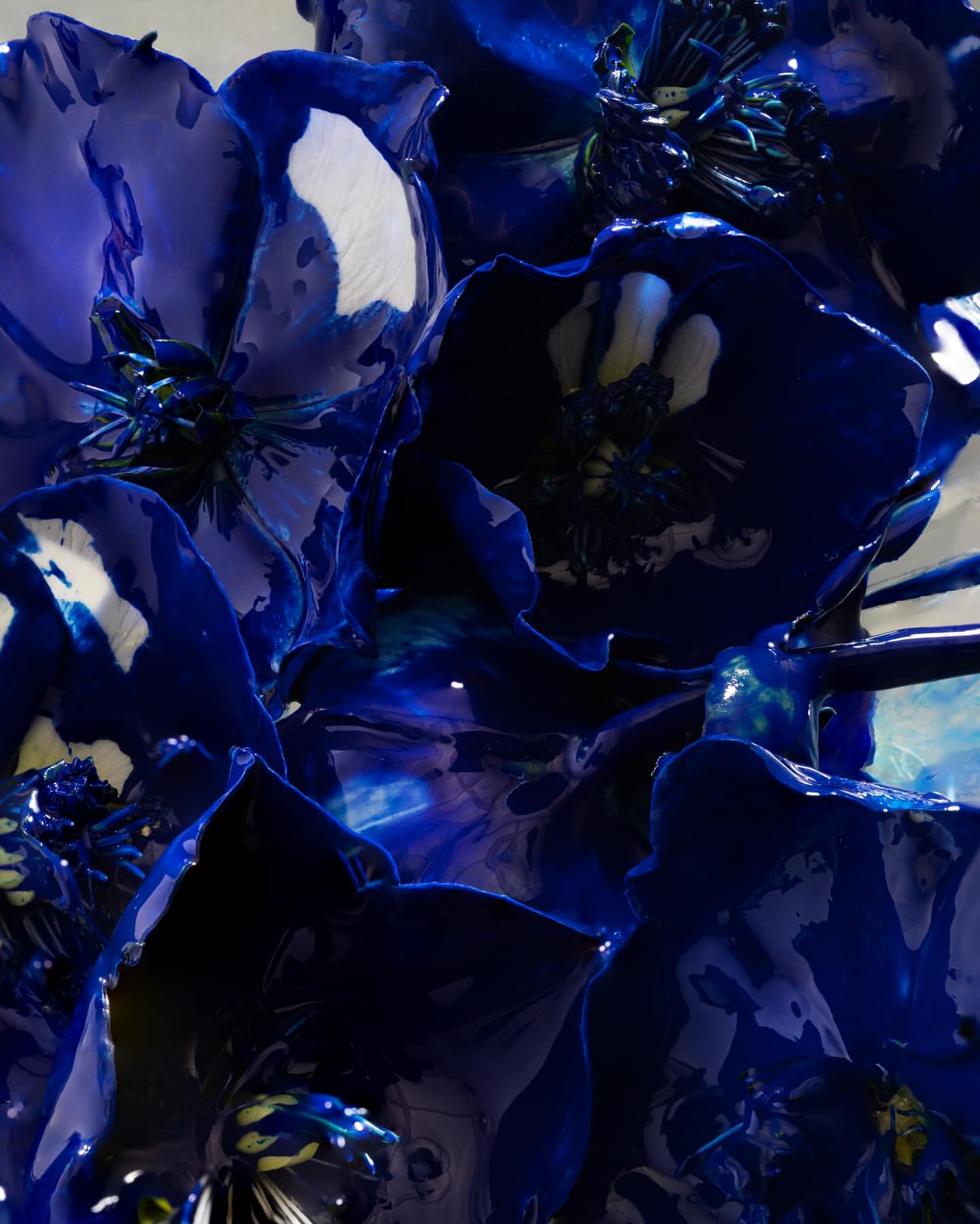 Abstract floral arrangement featuring large, glossy, deep blue flowers with white highlights. Close-up perspective reveals intricate details and textures.