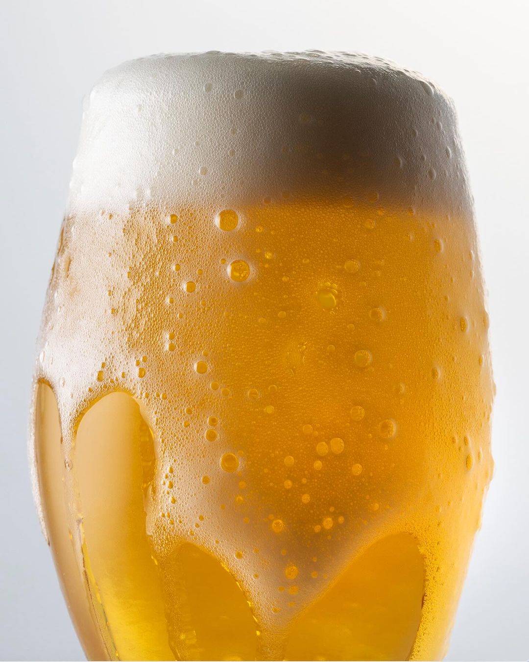Refreshing close-up of light beer in a glass, showcasing the foamy head and condensation on the glass surface against a bright backdrop.