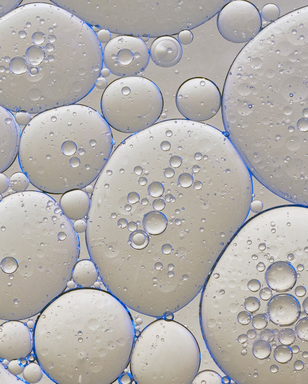 Close-up of numerous translucent liquid droplets with pale interior and blue edges, creating a visually intriguing abstract design.