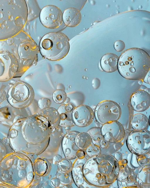 Macro view of spherical clear liquid bubbles, some with refraction, against a muted teal background, creating a mesmerizing visual effect.