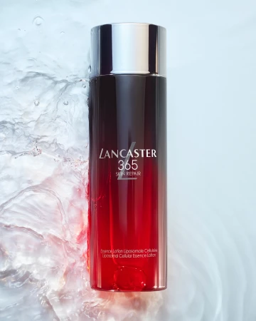 Lancaster 365 Skin Repair essence lotion bottle with black and red gradient, silver cap, and water splashes in a beauty shot.