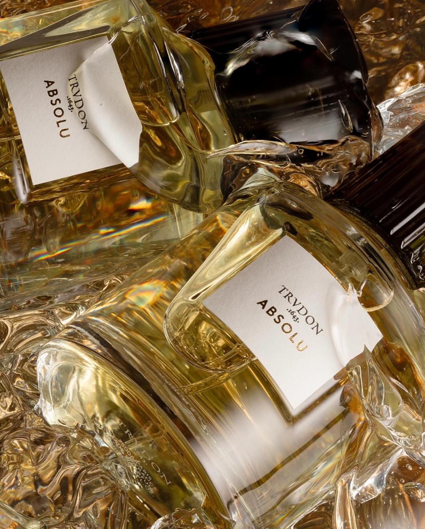 Overhead shot of multiple glass perfume bottles with white labels against a reflective gold background, with an elegant, high-end aesthetic.