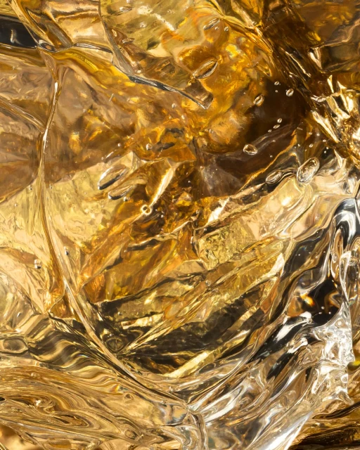 Close-up abstract photograph showcases textured amber liquid with rippling patterns, light reflections, and surface droplets.