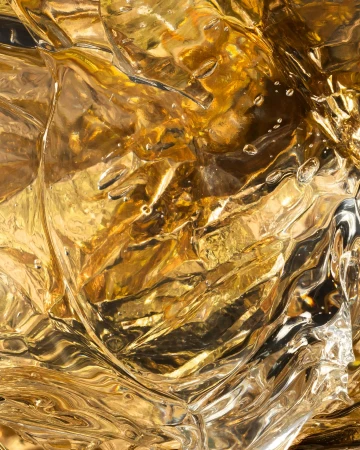 Close-up abstract photograph showcases textured amber liquid with rippling patterns, light reflections, and surface droplets.