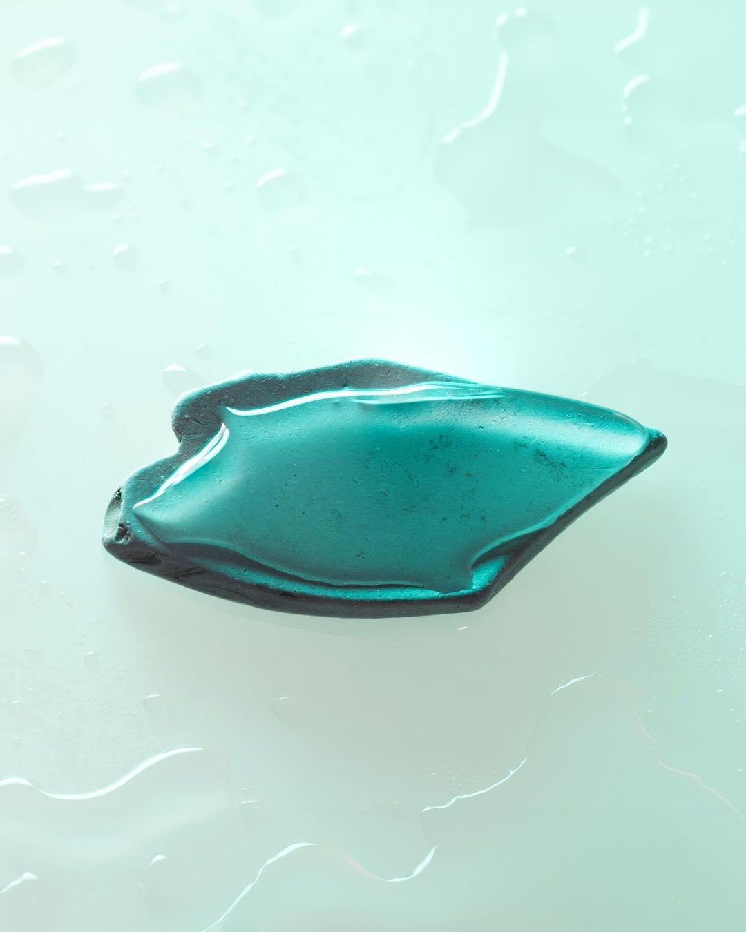 Close-up studio shot of teal cosmetic gel with water droplets on a light blue surface, capturing a fresh, minimalist beauty aesthetic.