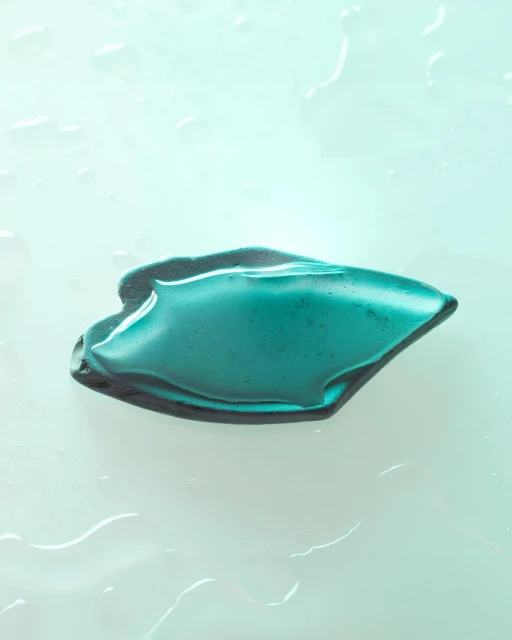 Close-up studio shot of teal cosmetic gel with water droplets on a light blue surface, capturing a fresh, minimalist beauty aesthetic.